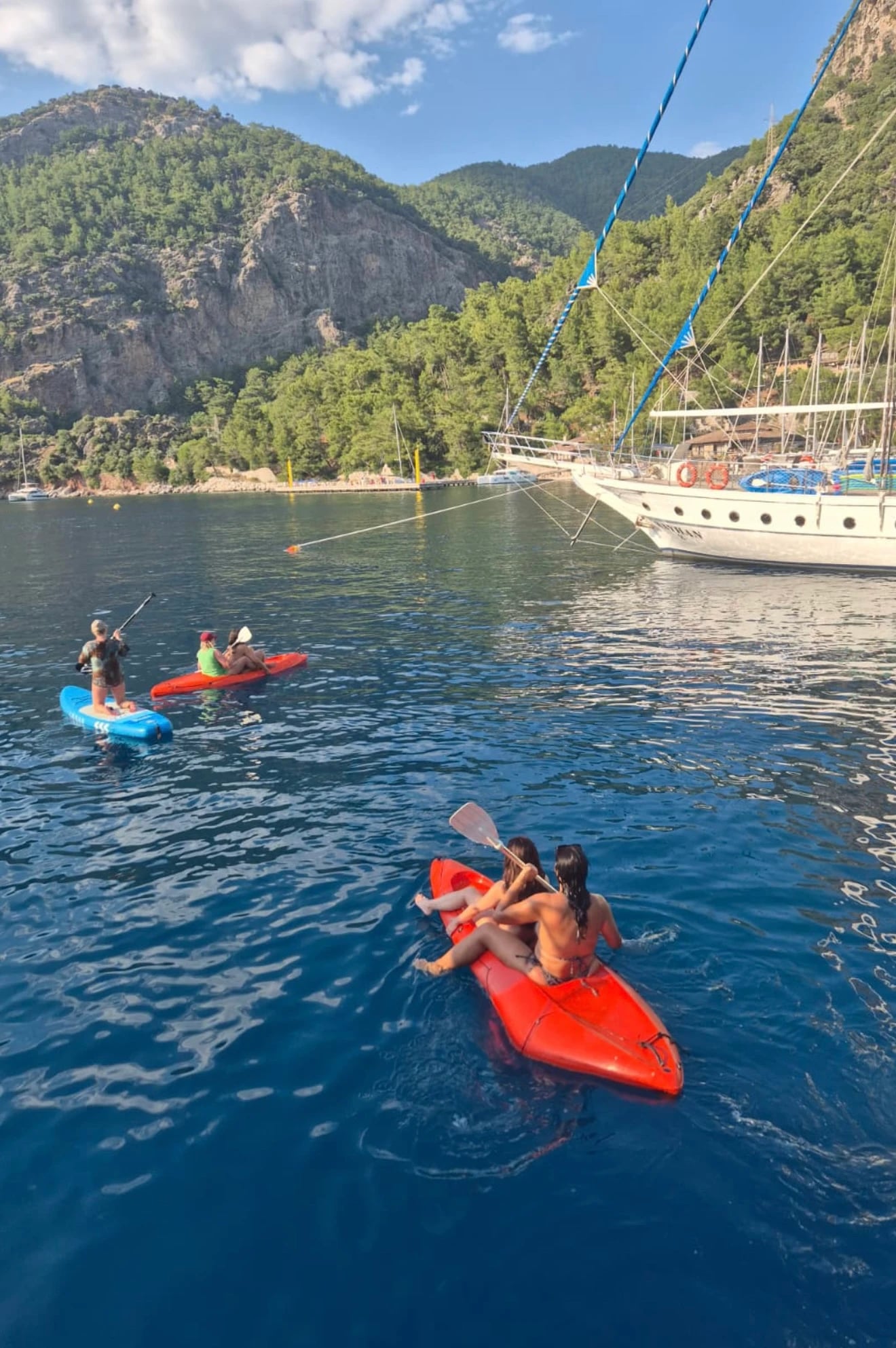Frauen paddeln in Kajak und auf Stand-up-Paddle-Boards durch eine ruhige, tiefblaue Bucht neben der Yacht.