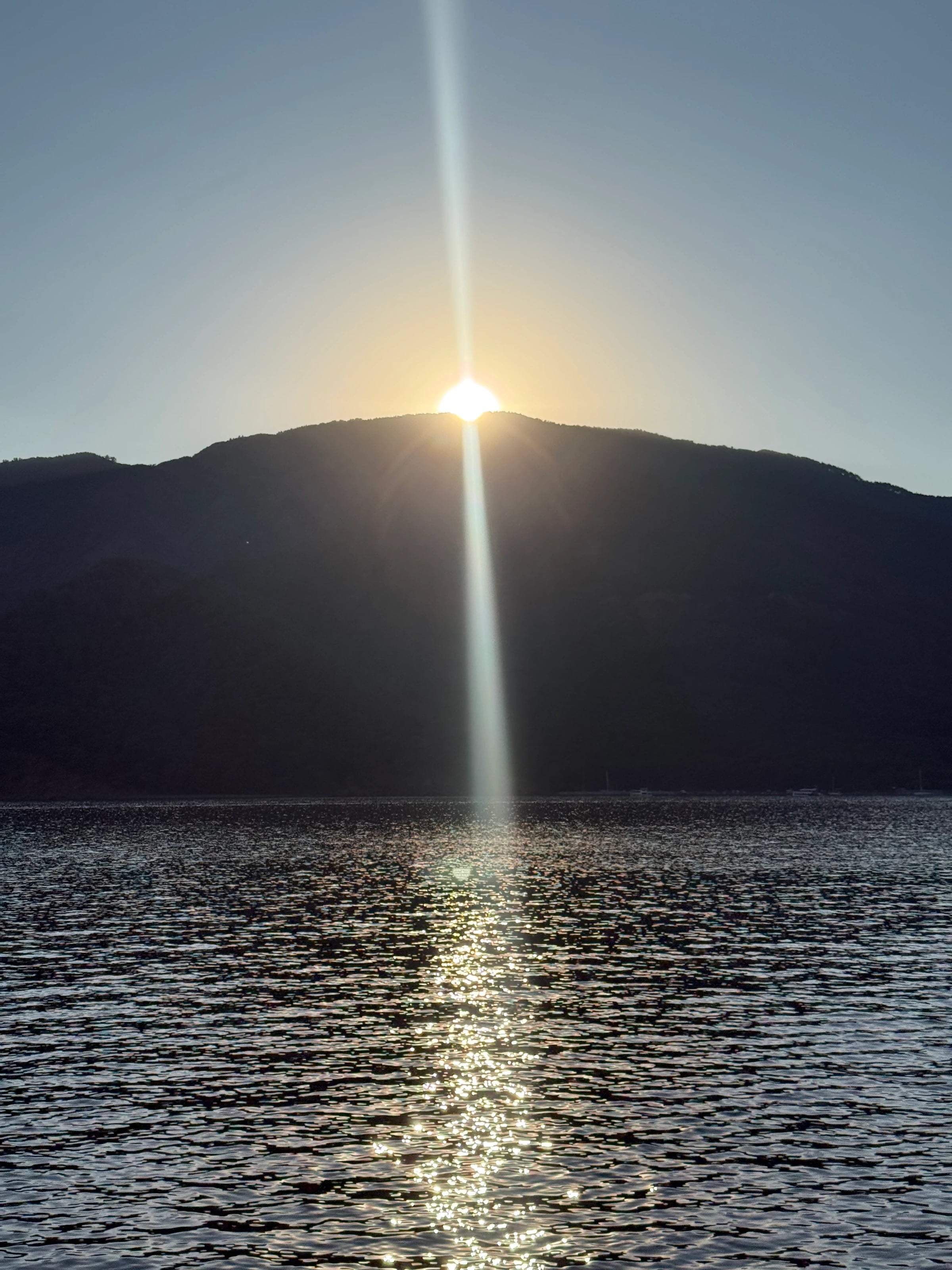Die Sonne geht hinter einem dunklen Bergrücken auf und spiegelt sich im glitzernden Wasser der Bucht.