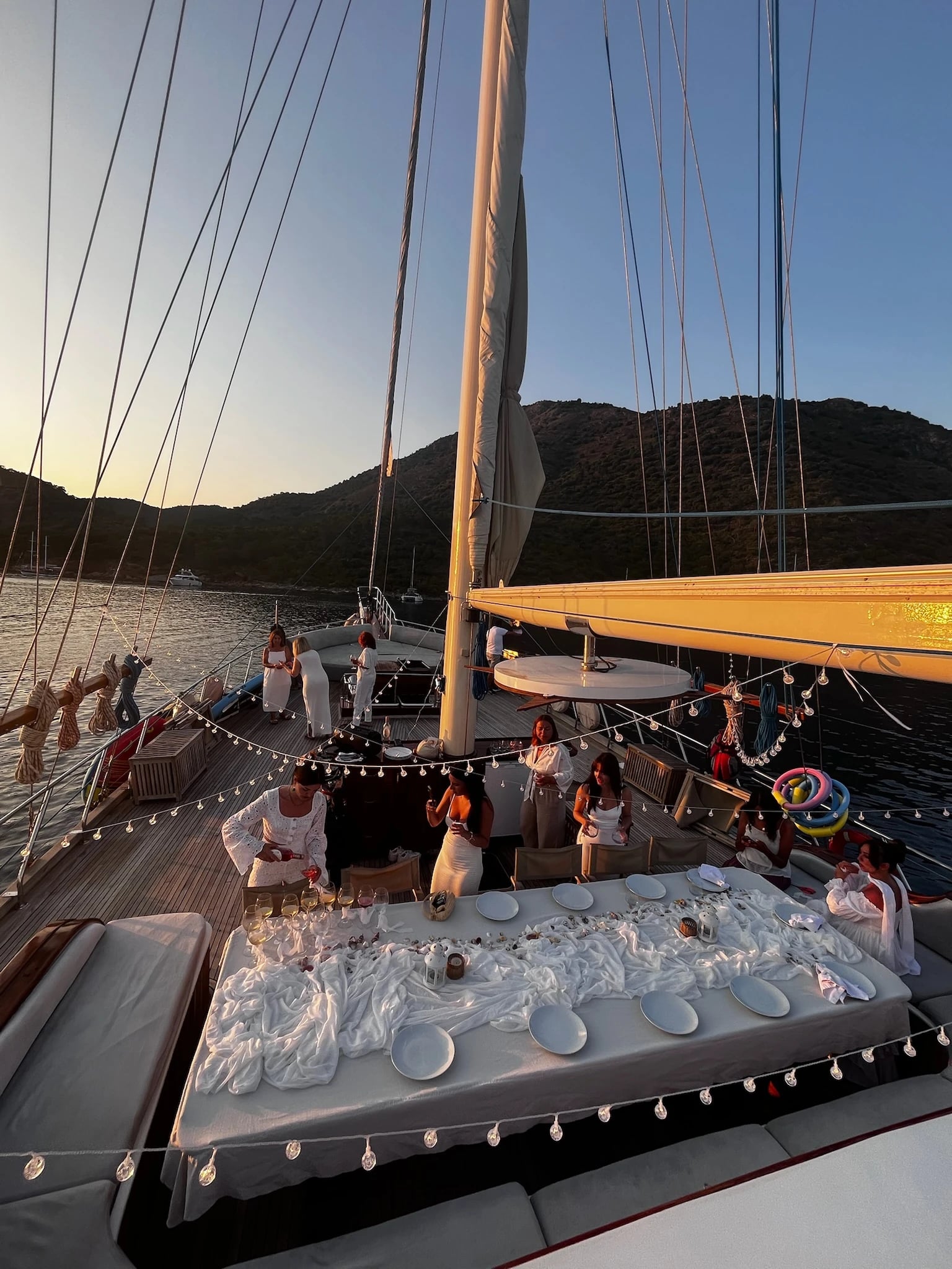 Die Frauen in Weiß bereiten auf dem Deck unter Lichterketten die große Abendtafel im goldenen Licht vor.