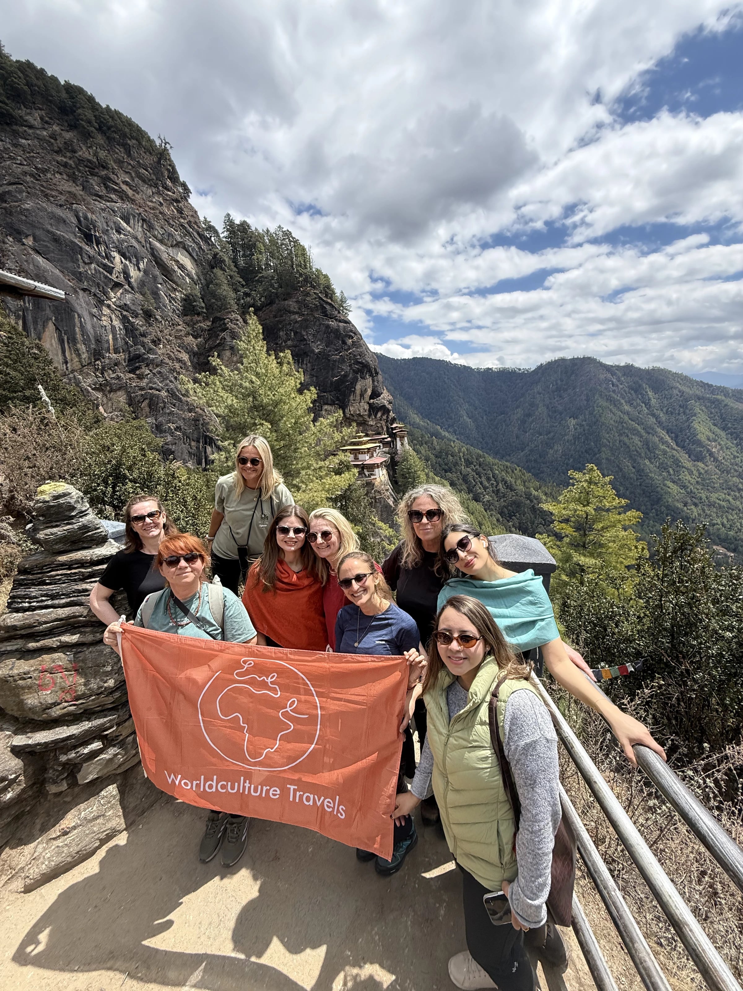 Die Reisegruppe hält die orangefarbene Worldculture-Travels-Fahne vor dem Tigernest Kloster.