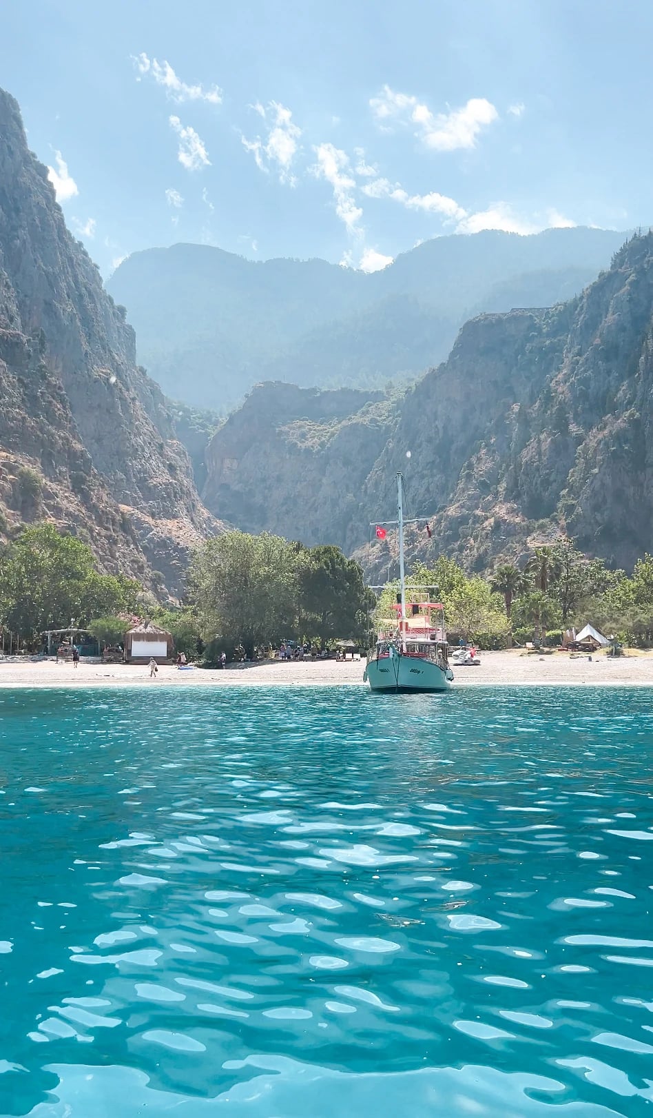 Blick vom türkisfarbenen Wasser auf den Strand von Butterfly Valley zwischen steilen Felswänden.