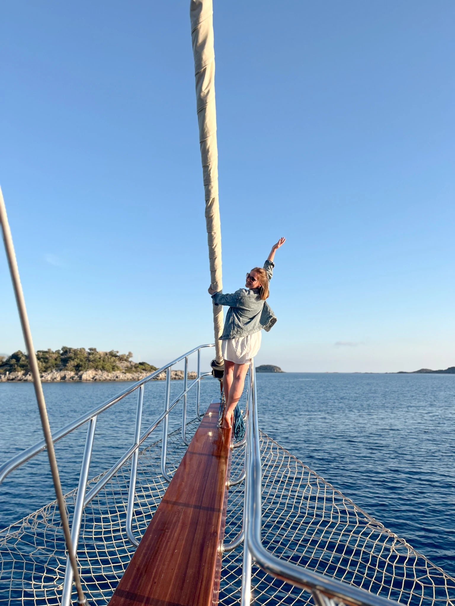 Saskia in Jeansjacke winkt fröhlich vom Bug der Gulet, dahinter das ruhige blaue Meer.