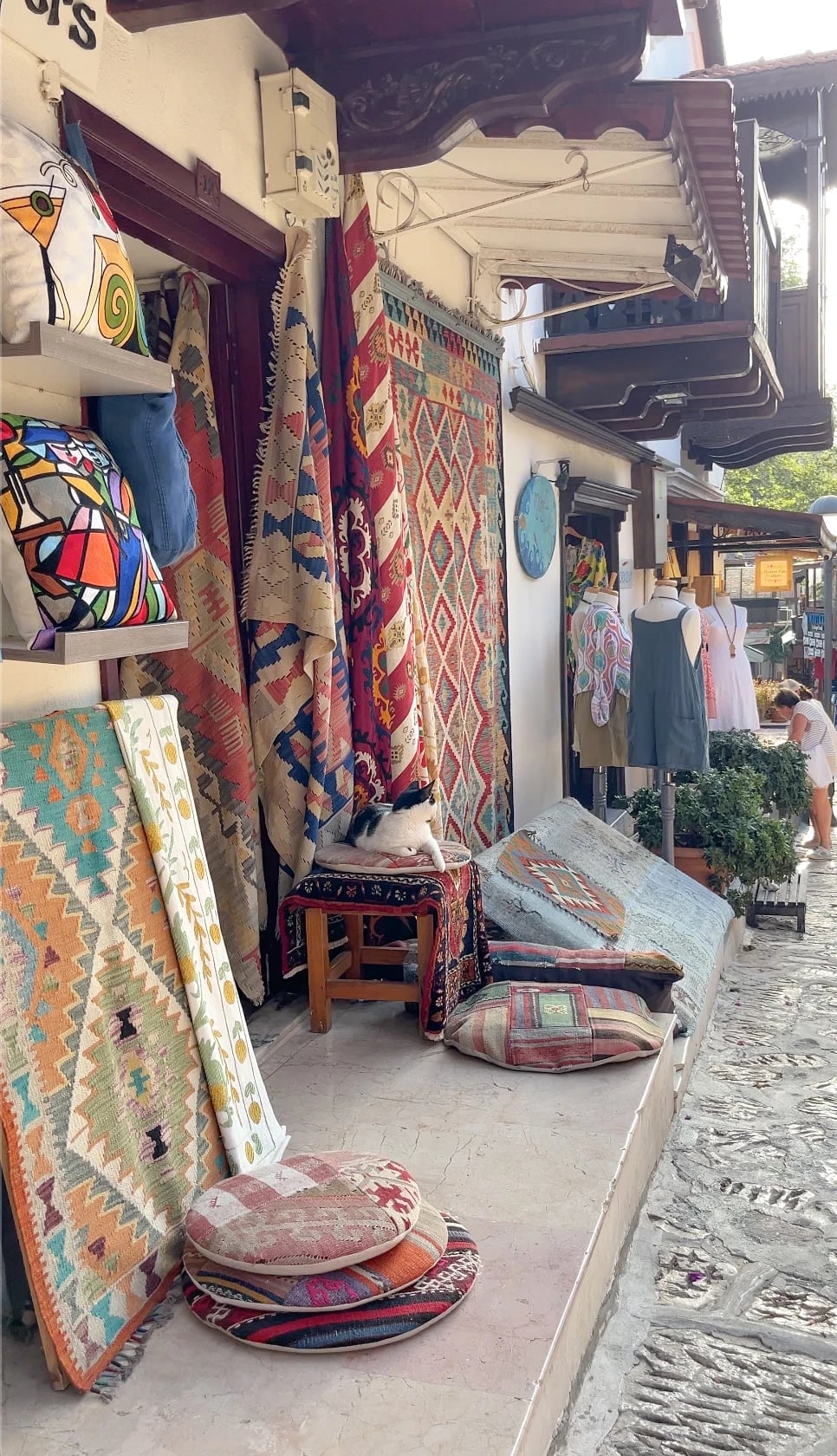Bunte Kelimteppiche vor einem kleinen Laden in der Altstadt, auf einem Hocker döst eine Katze.