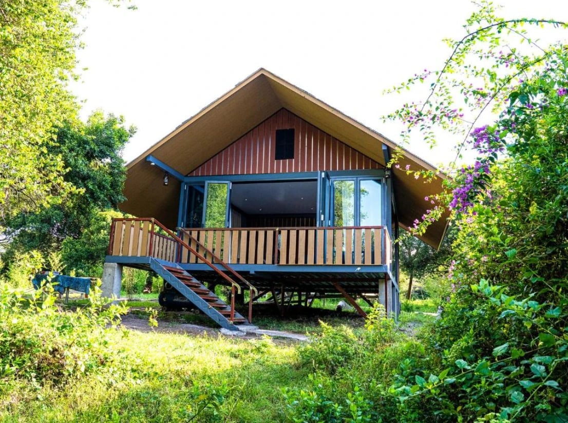 Ein Holzchalet auf Stelzen mit Terrasse, umgeben von Grün und blühender Bougainvillea.