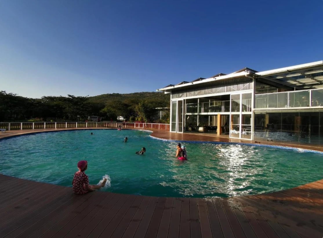 Gäste baden im runden Pool der Lodge vor dem gläsernen Haupthaus.