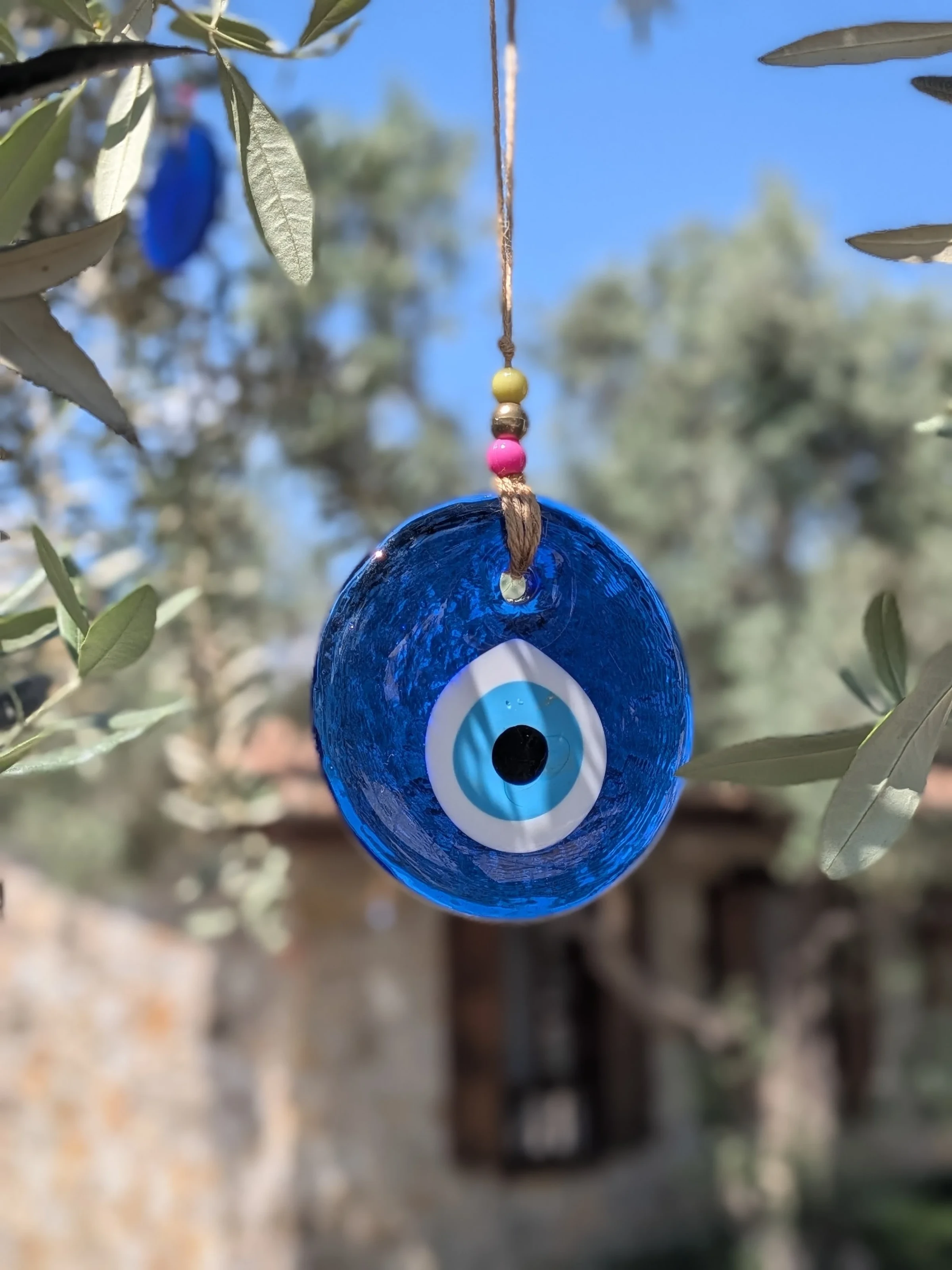 Ein blaues Nazar-Auge aus Glas hängt an einem Band in den Zweigen eines Olivenbaums.