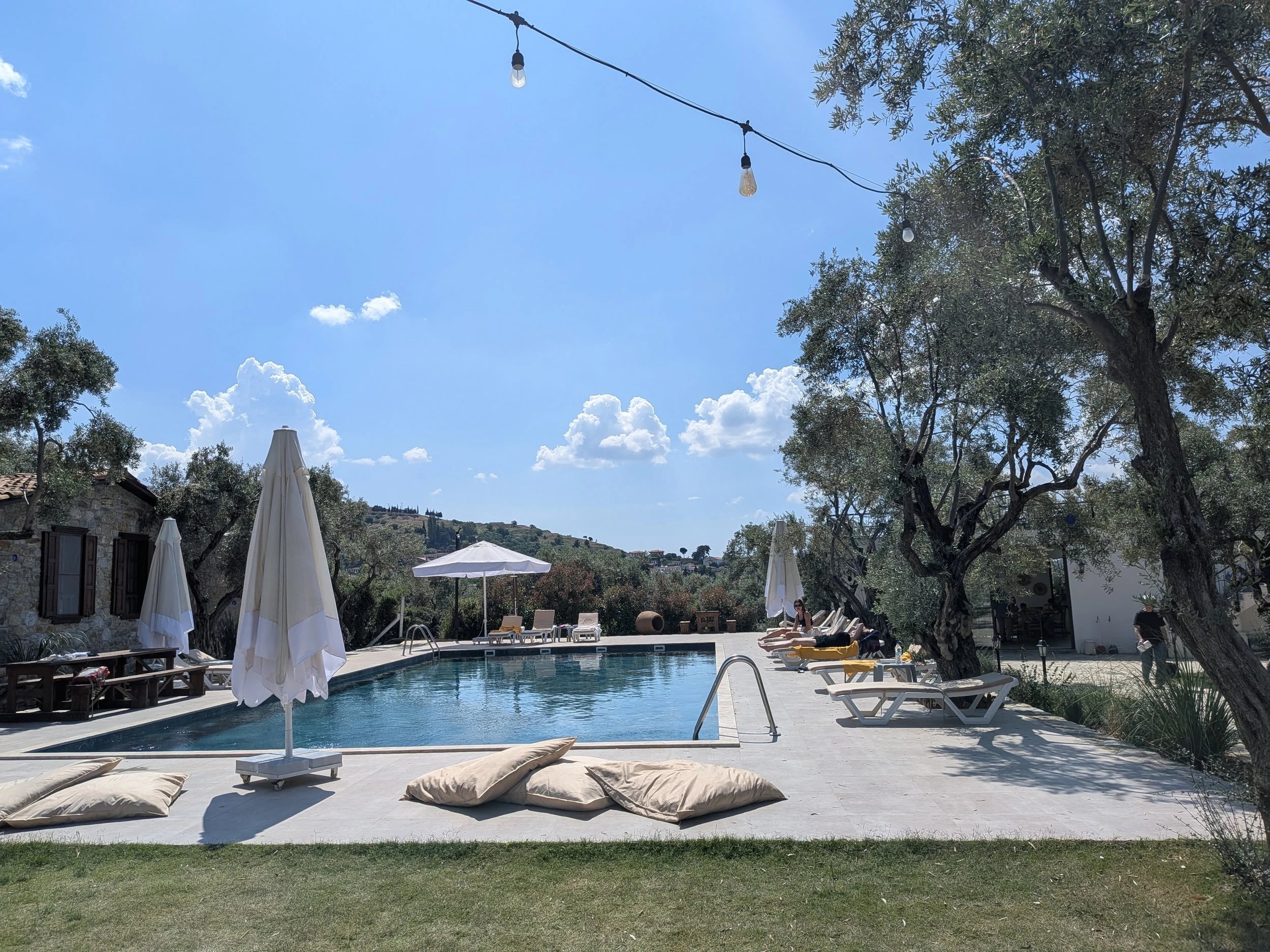 Lichterketten spannen sich über den Pool, im Gras davor liegen große Sitzkissen.