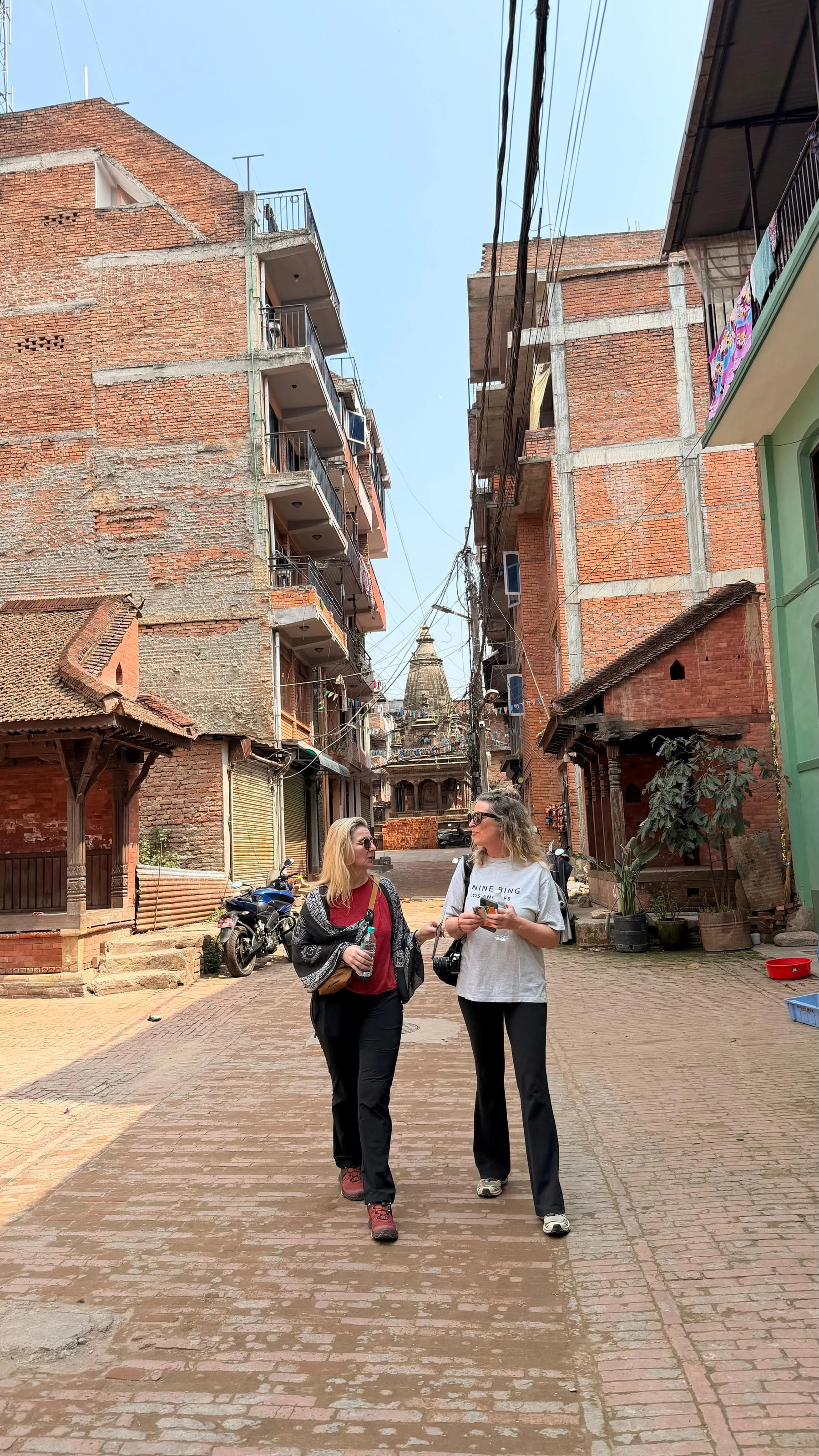 Zwei Reisende schlendern durch eine schmale Gasse in Bhaktapur mit Tempelspitze im Hintergrund.