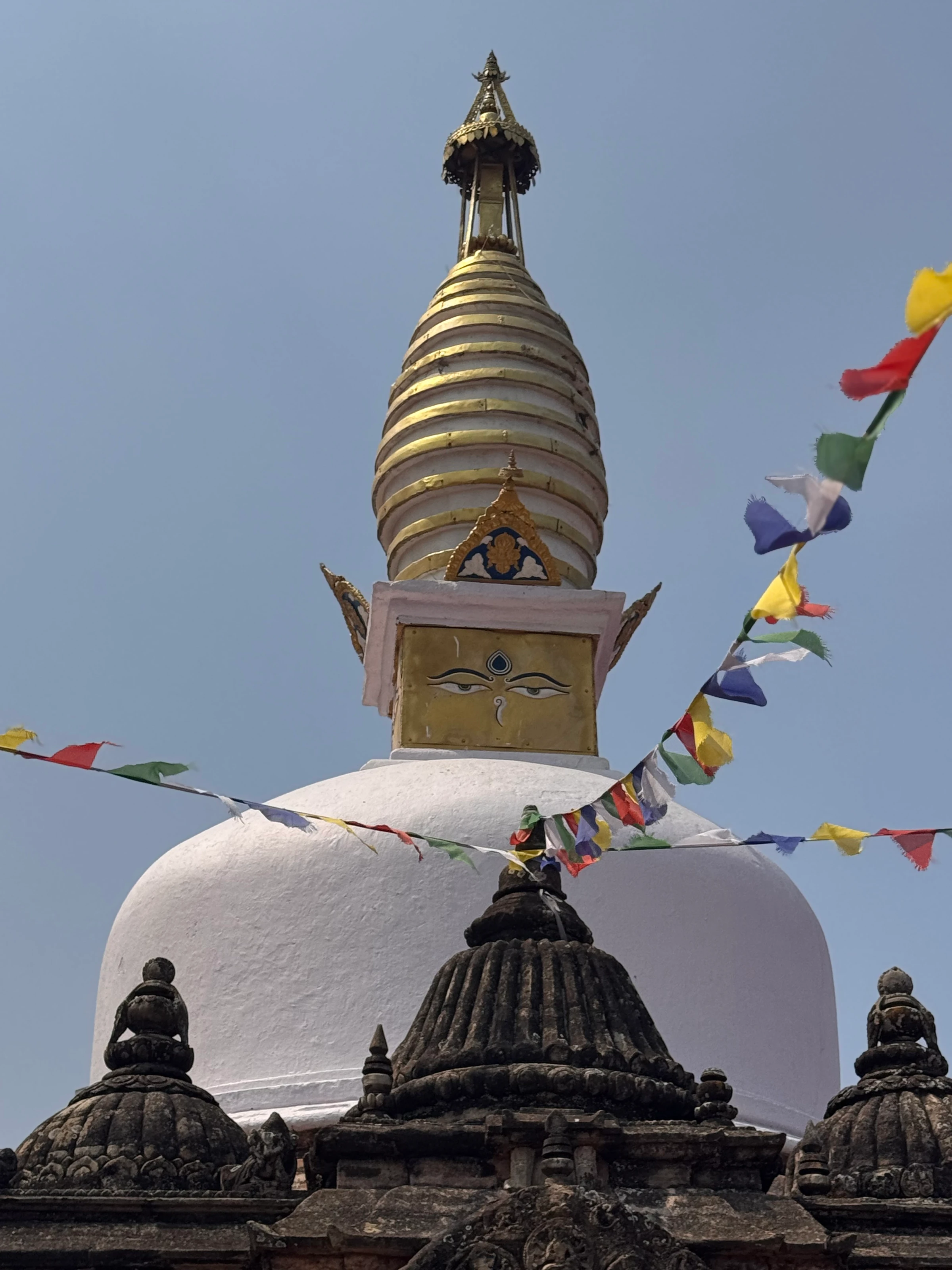 Nahaufnahme der goldenen Turmspitze einer Stupa mit den gemalten Buddha-Augen.