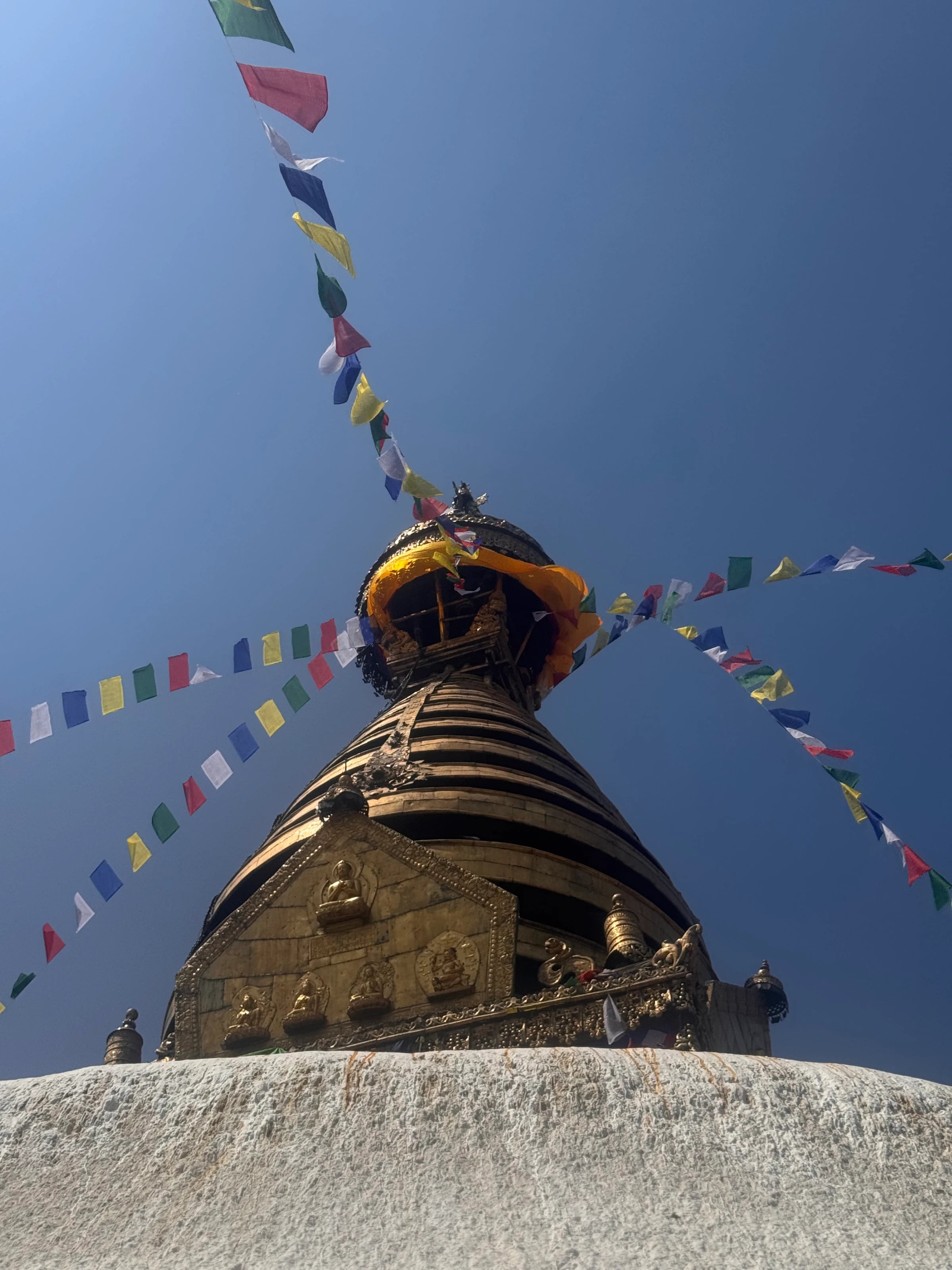 Blick von unten auf die goldene Spitze der Swayambhunath-Stupa mit bunten Gebetsfahnen vor blauem Himmel.