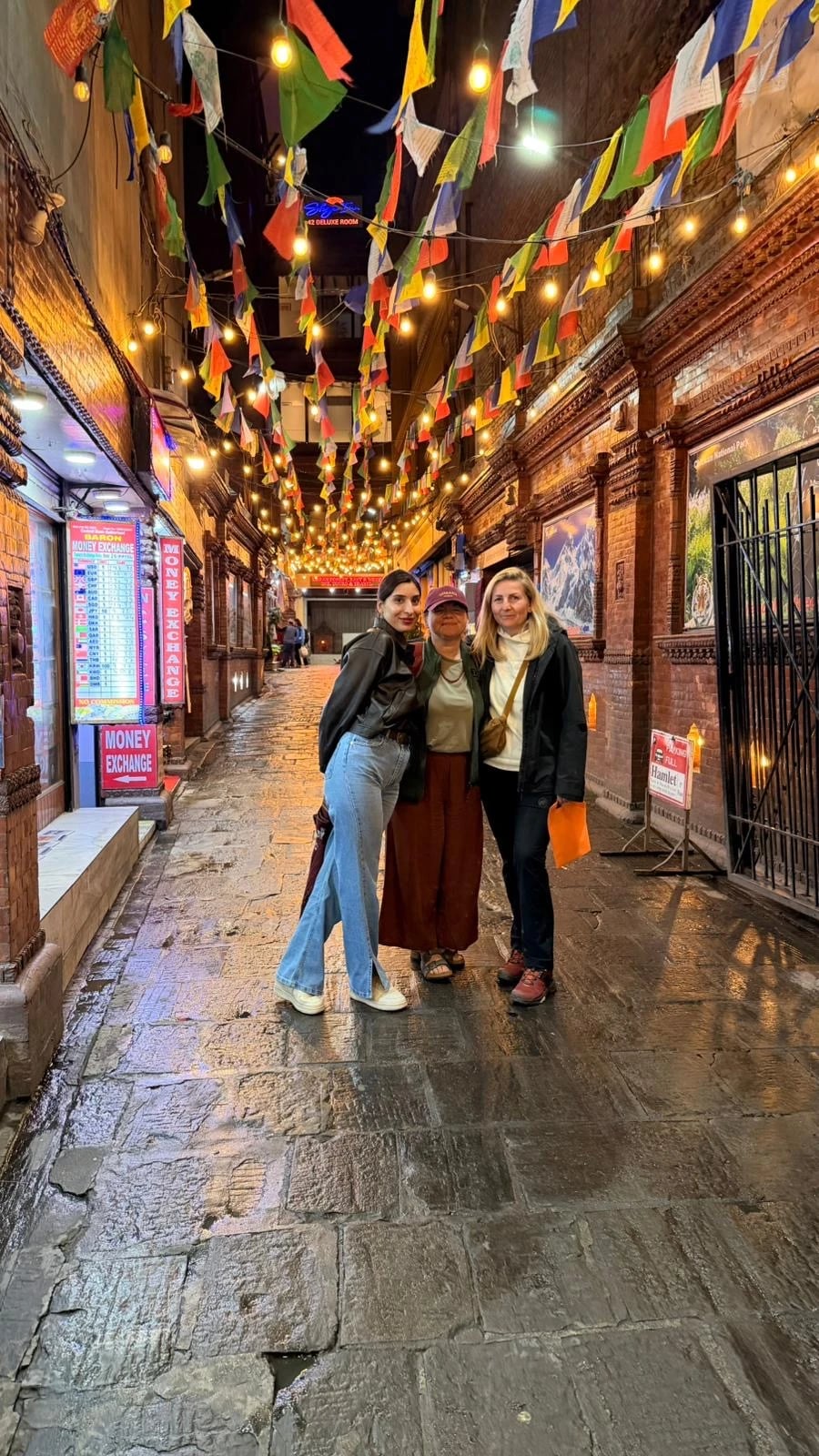 Drei Reisende stehen abends in einer beleuchteten Gasse in Thamel, über ihnen bunte Gebetsfahnen.
