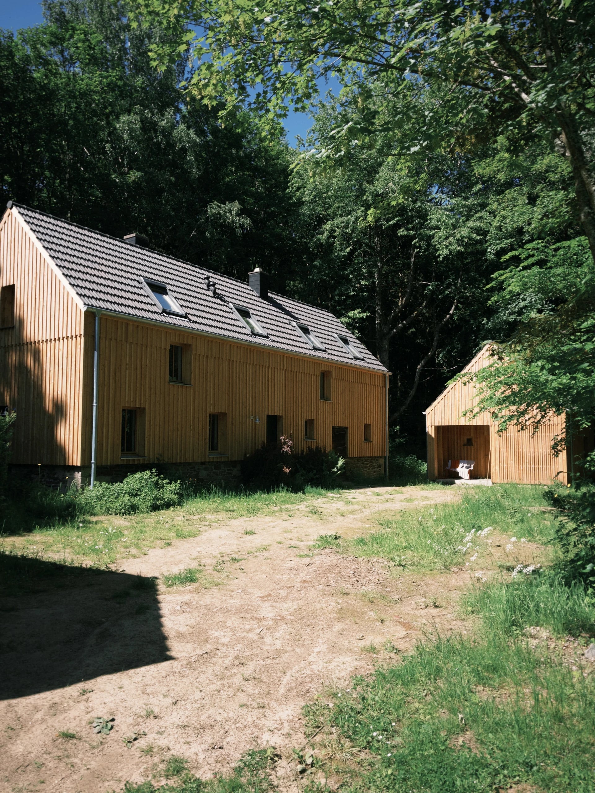 Der Hof aus Holz mit Nebengebäude, umgeben von Bäumen und einer Wiese in der Eifel.