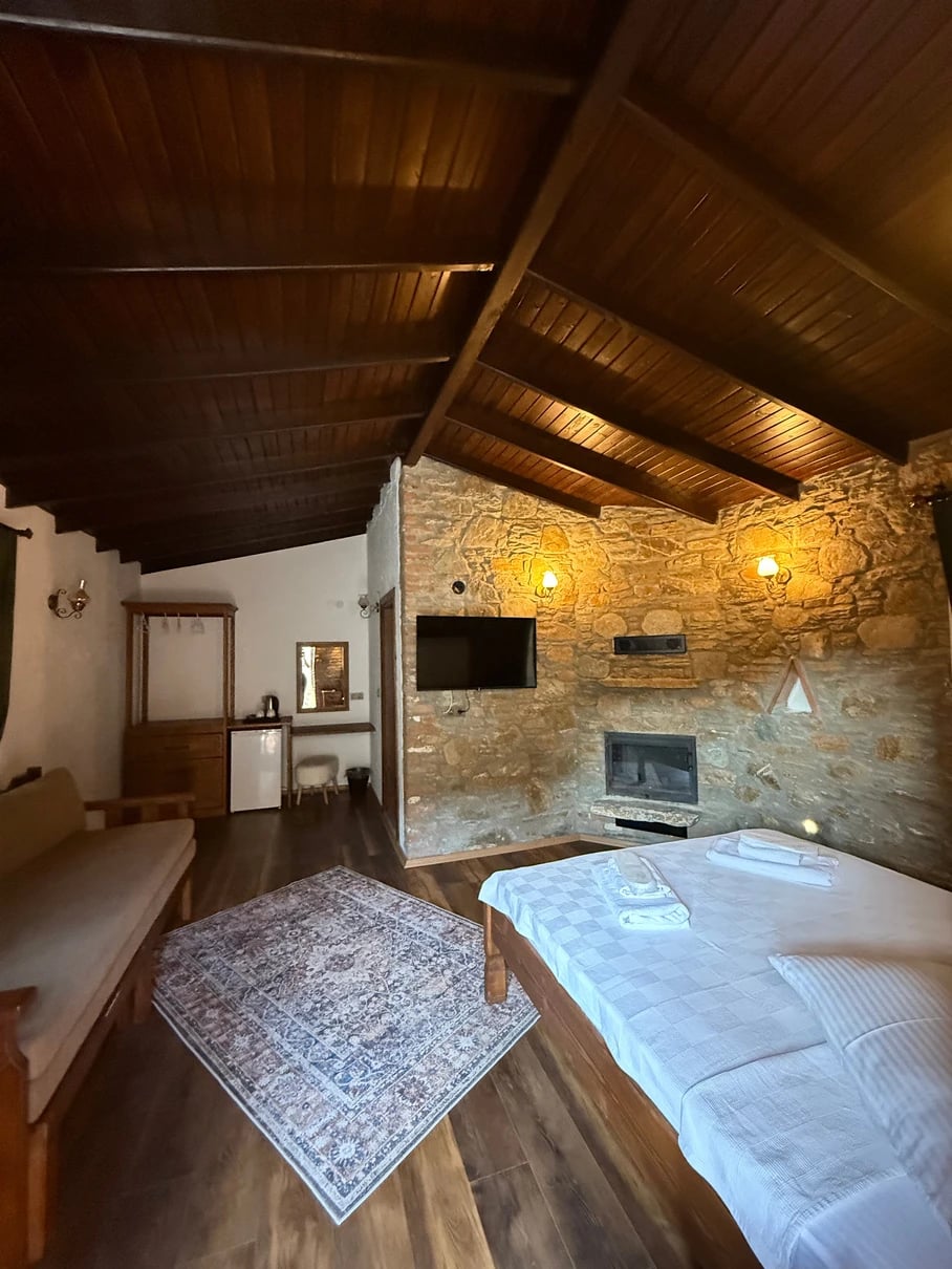 Zimmer im Steinhaus mit Holzdecke, Kamin, Fernseher, Sofa und Doppelbett.