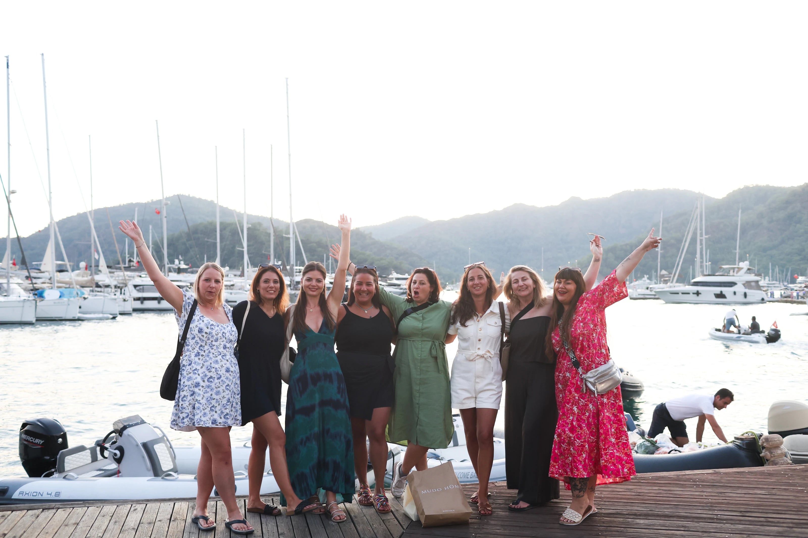 Gruppe Frauen jubelt mit erhobenen Armen auf dem Steg vor Bergkulisse.