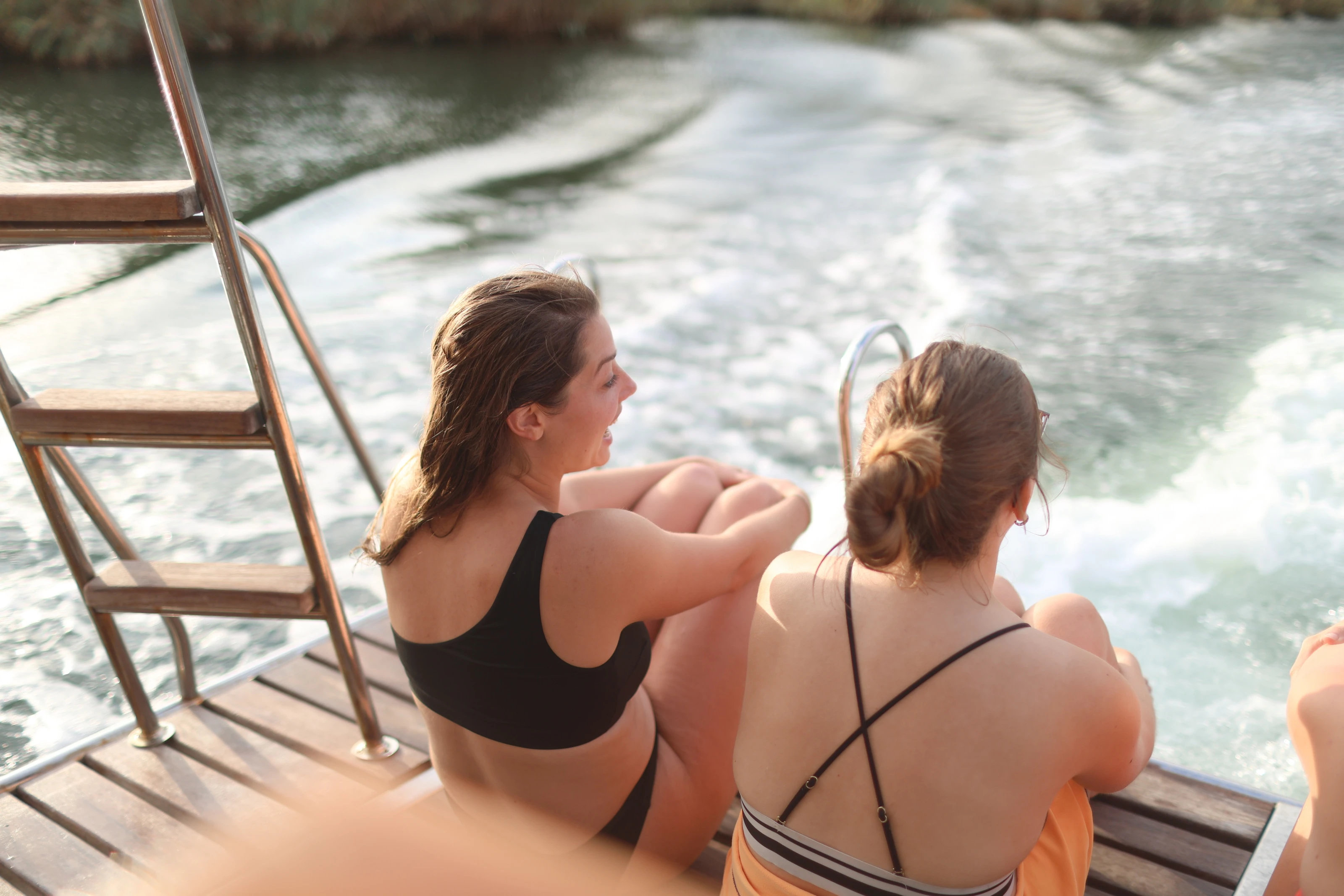 Zwei Frauen sitzen am Heck des Schiffs und blicken gemeinsam auf das Kielwasser.