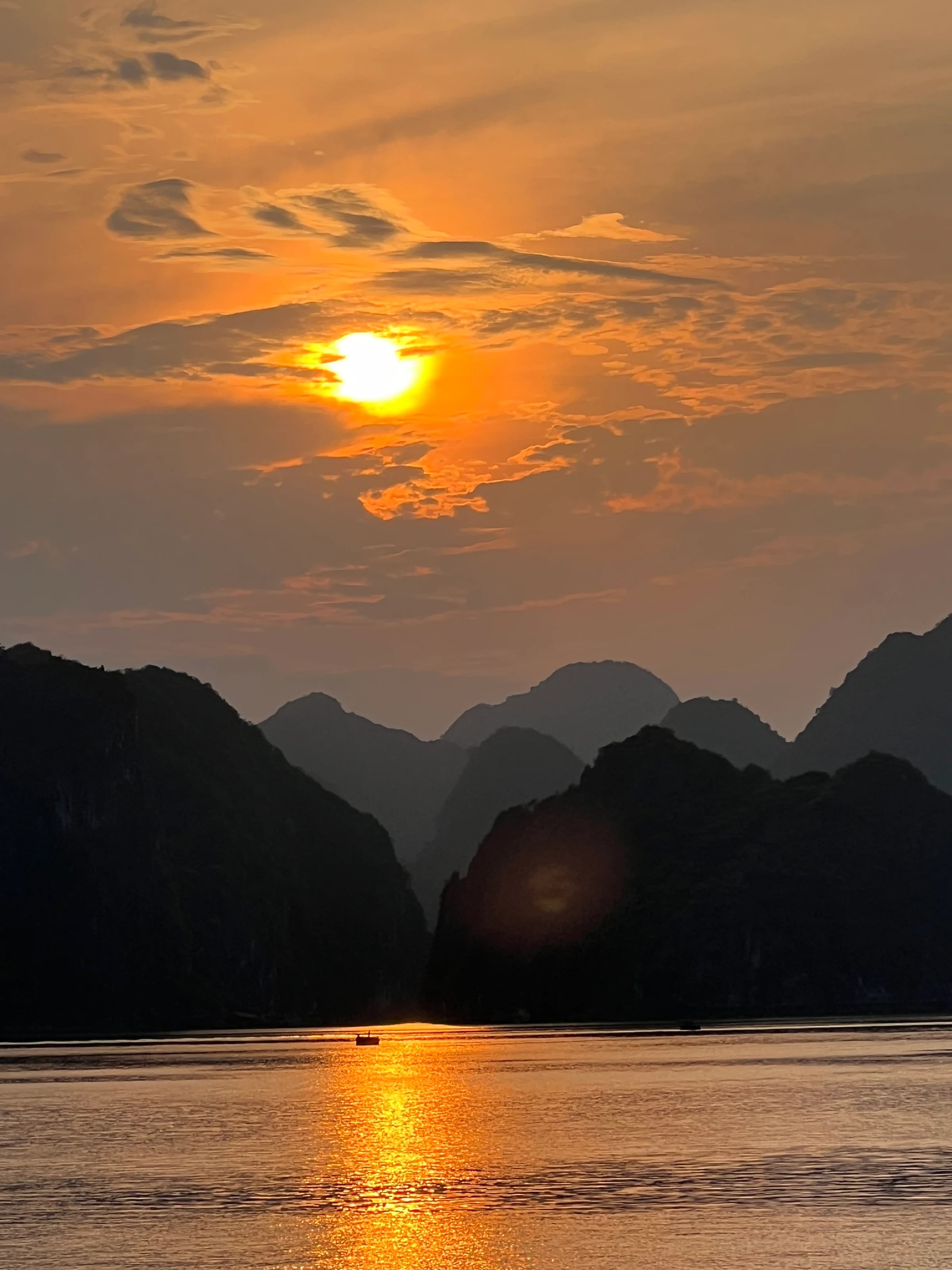 Die Sonne geht hinter den Karstfelsen der Lan-Ha-Bucht unter und spiegelt sich golden im Wasser.