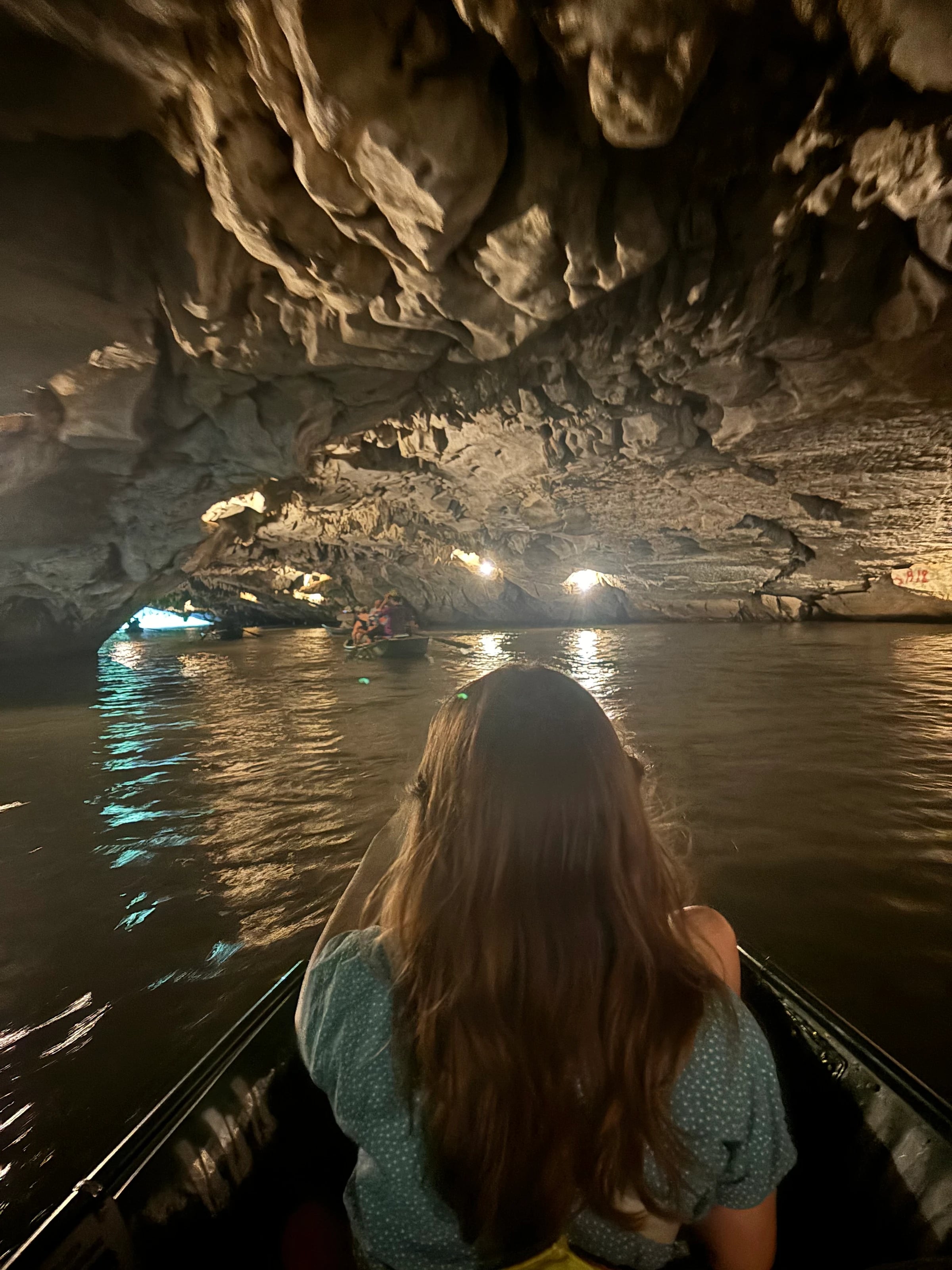 Eine Frau sitzt vorn im Ruderboot und fährt durch eine beleuchtete Kalksteinhöhle in Tam Coc.