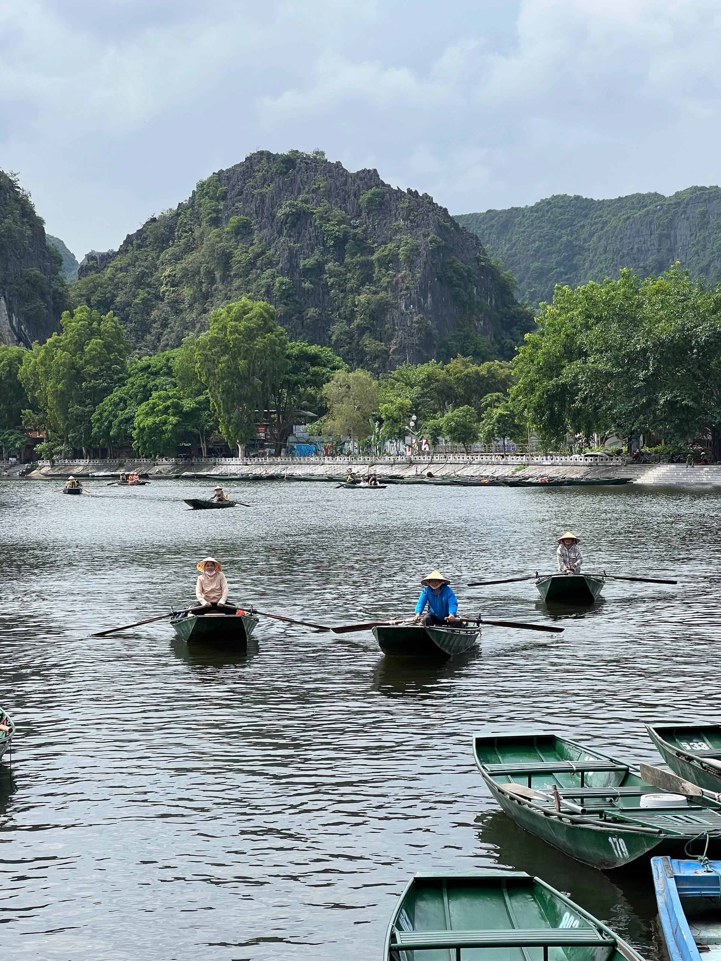 Ruderinnen mit Strohhüten auf dem Fluss in Tam Coc, dahinter grüne Karstberge.