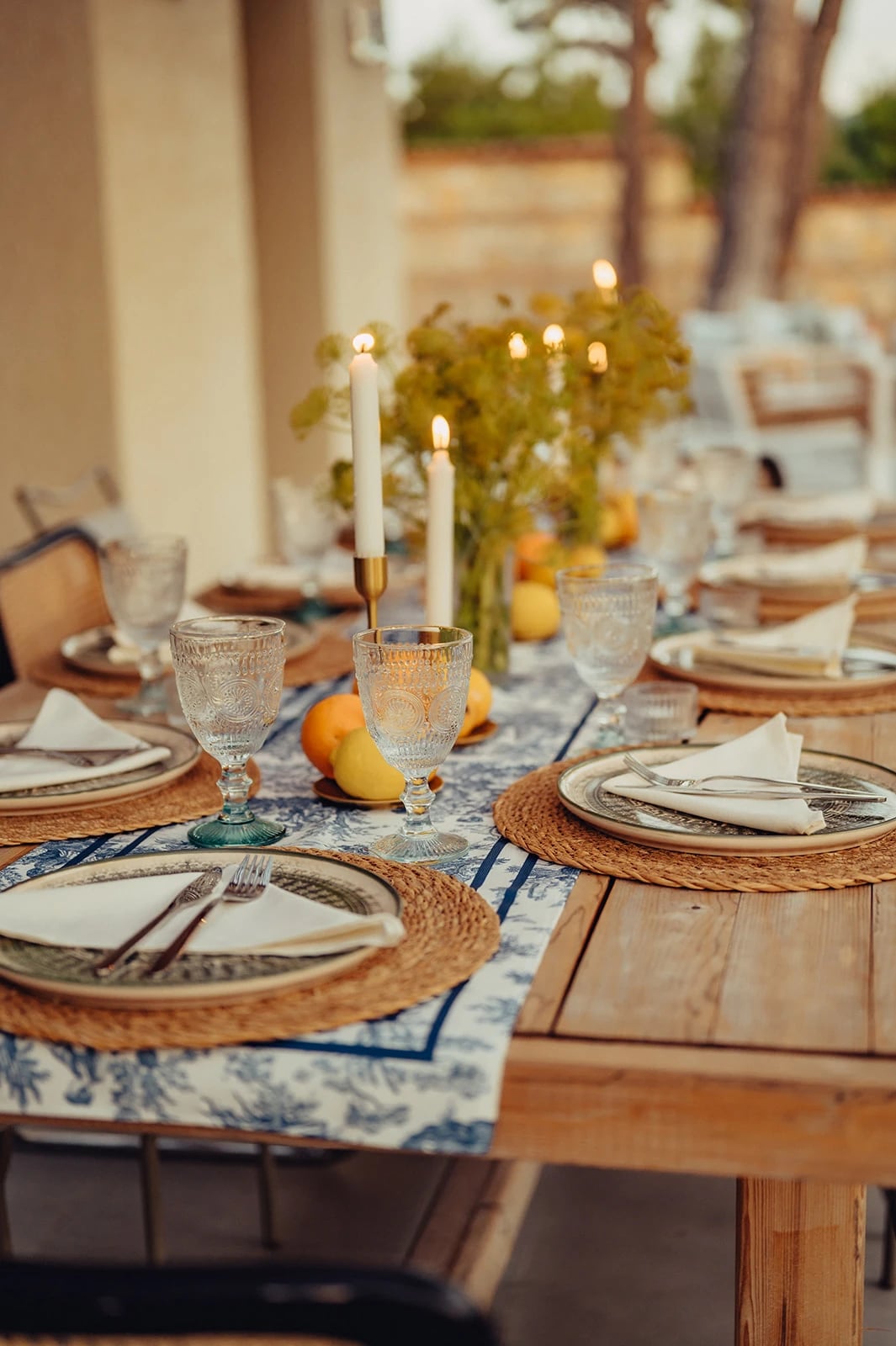 Eine lange gedeckte Tafel mit Kerzen, Zitrusfrüchten und Blumen im Freien.