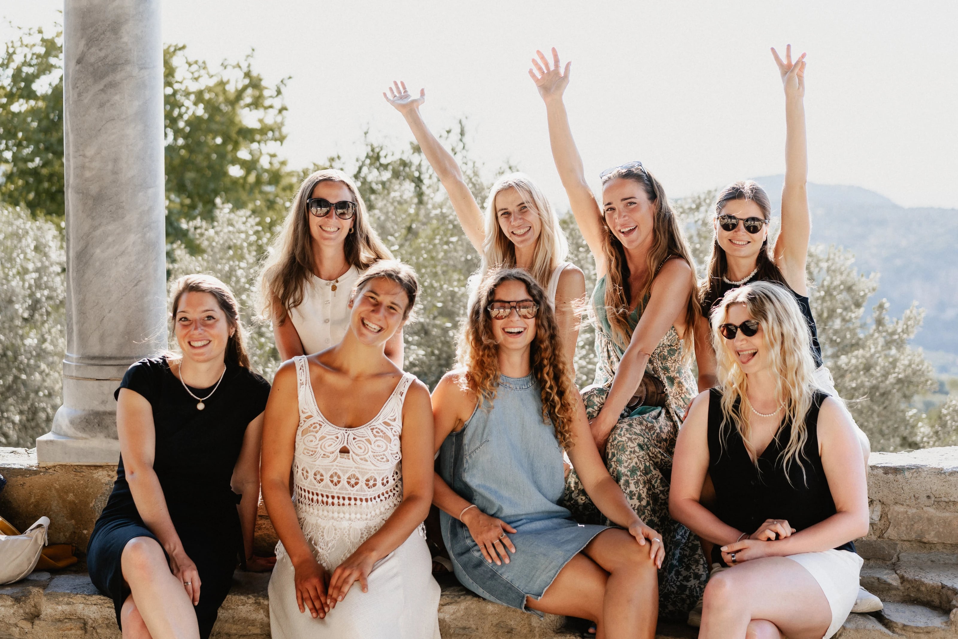 Eine fröhliche Gruppe von acht Frauen posiert lachend für ein Gruppenfoto im Freien.