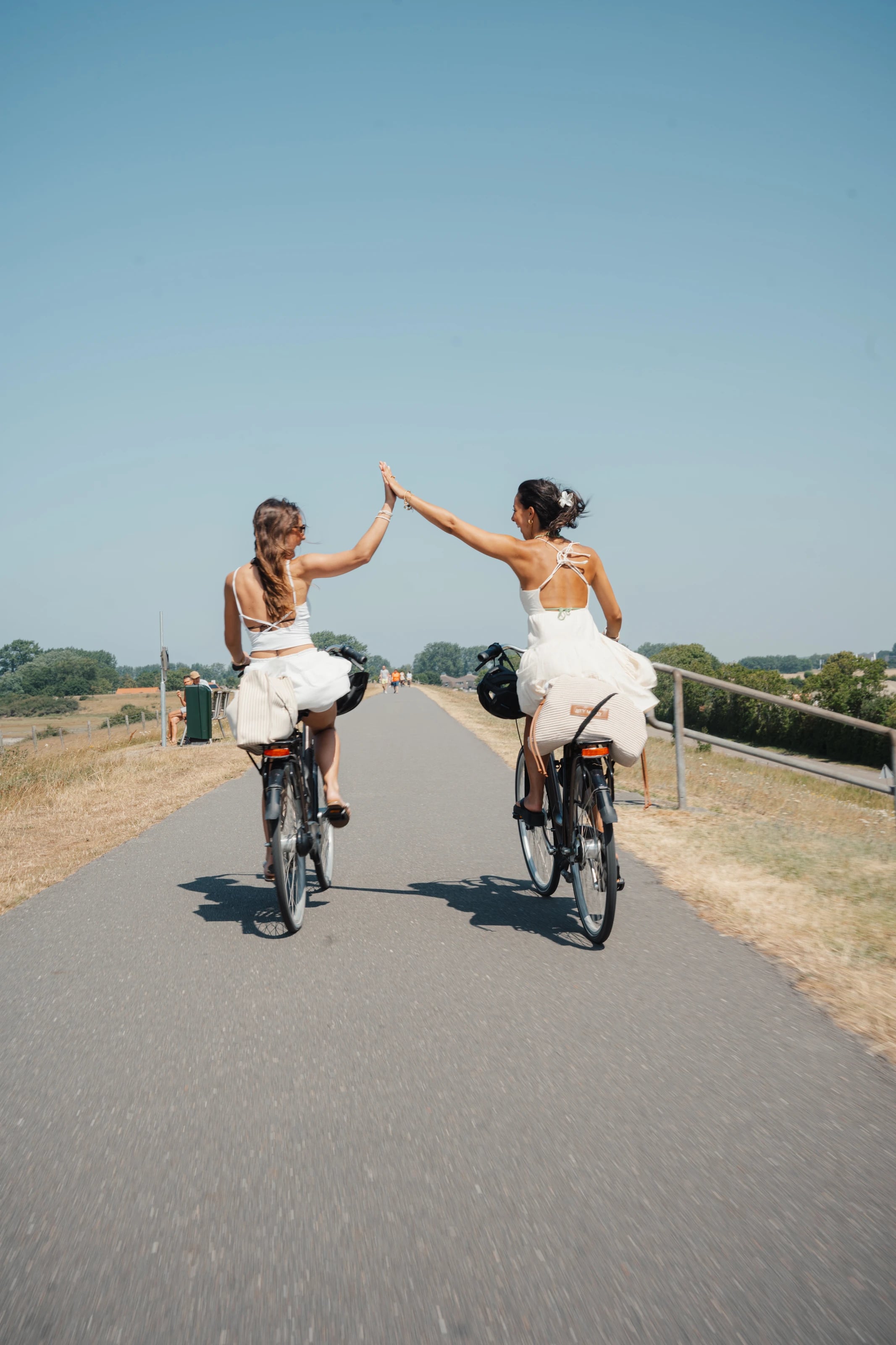 Zwei Radfahrerinnen klatschen sich auf einem geraden Weg ab.