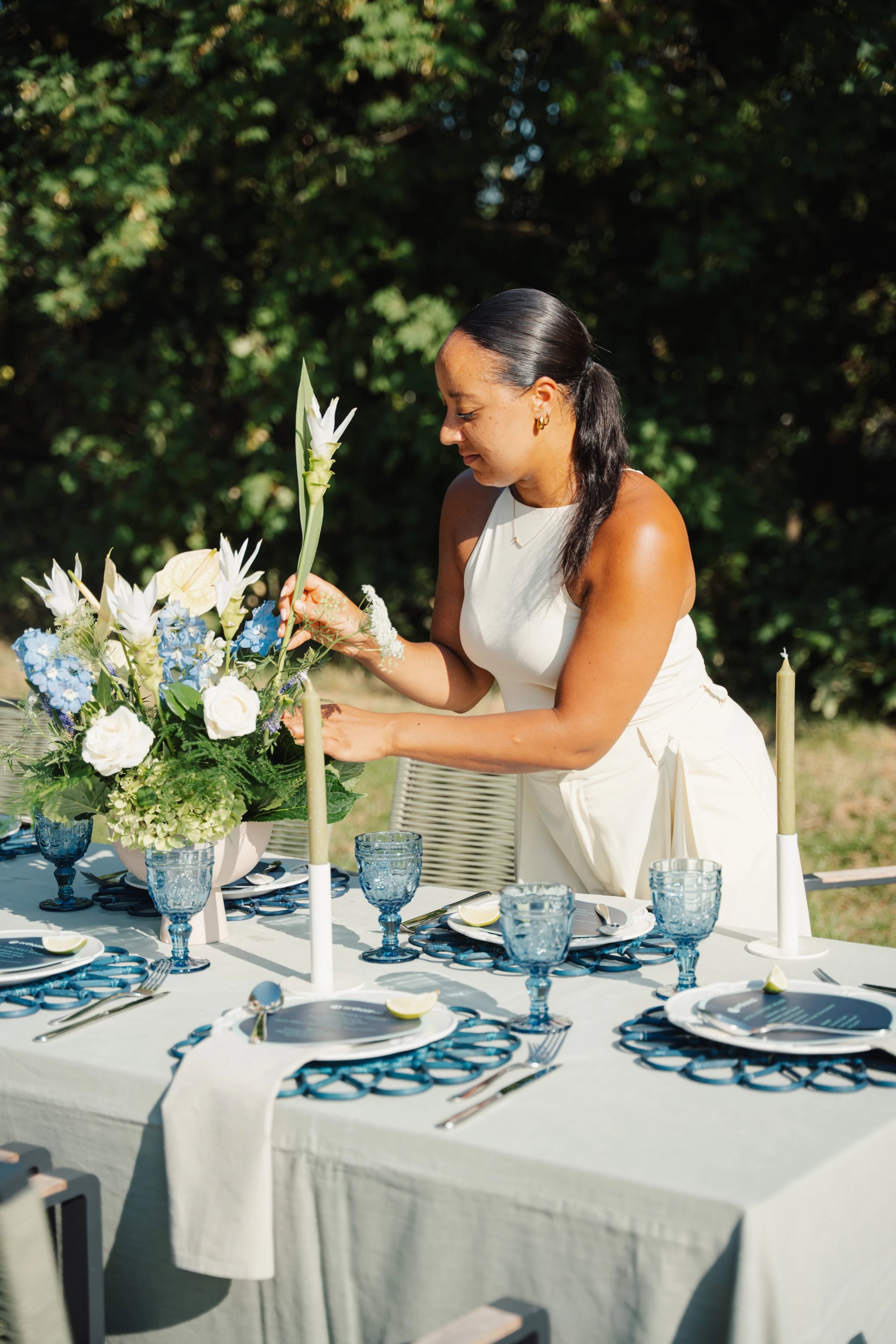 Eine Frau arrangiert einen Blumenstrauß an einer festlich gedeckten Tafel im Freien.