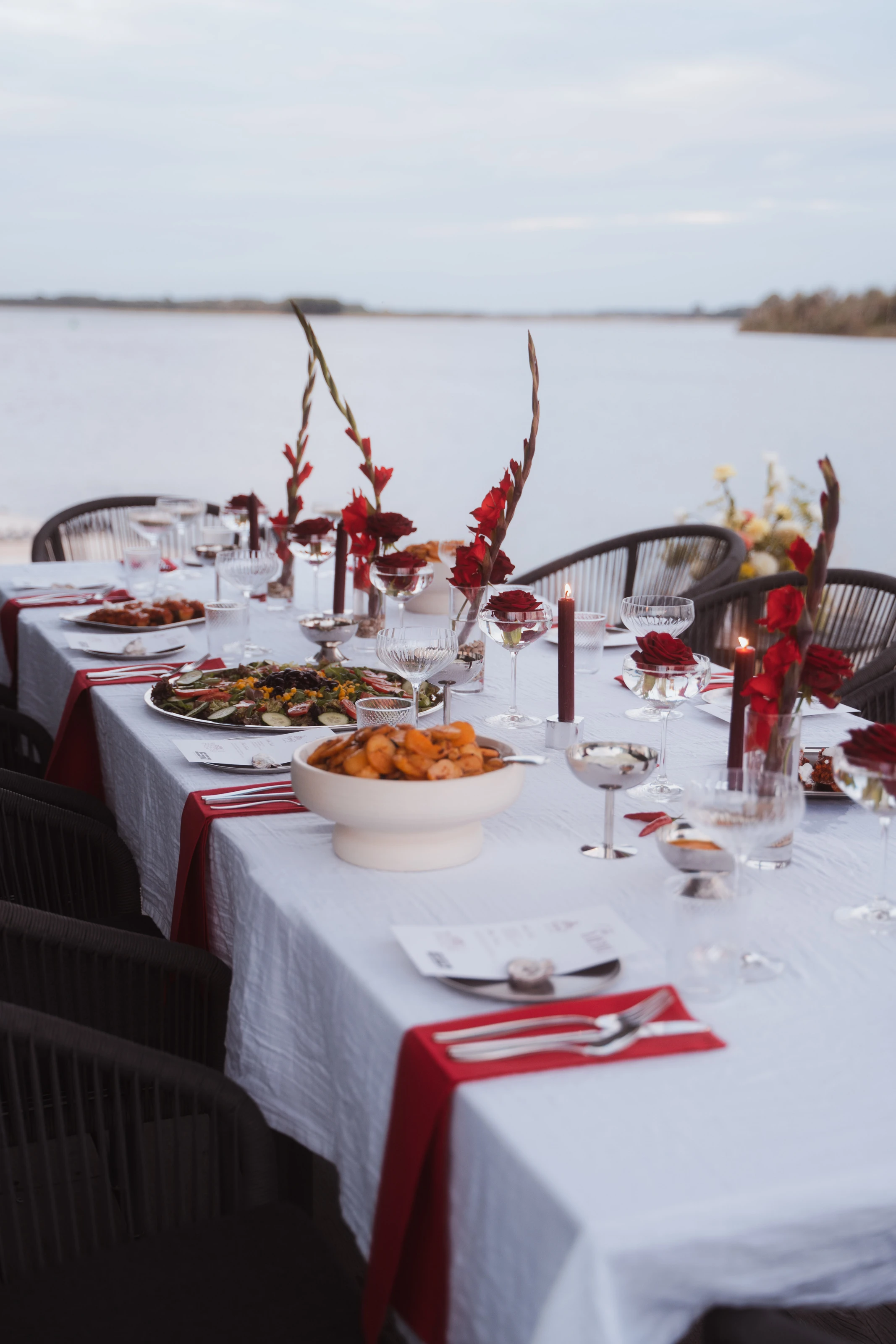 Festlich gedeckte Tafel am Wasser mit roten Rosen, Kerzen und Vorspeisen.
