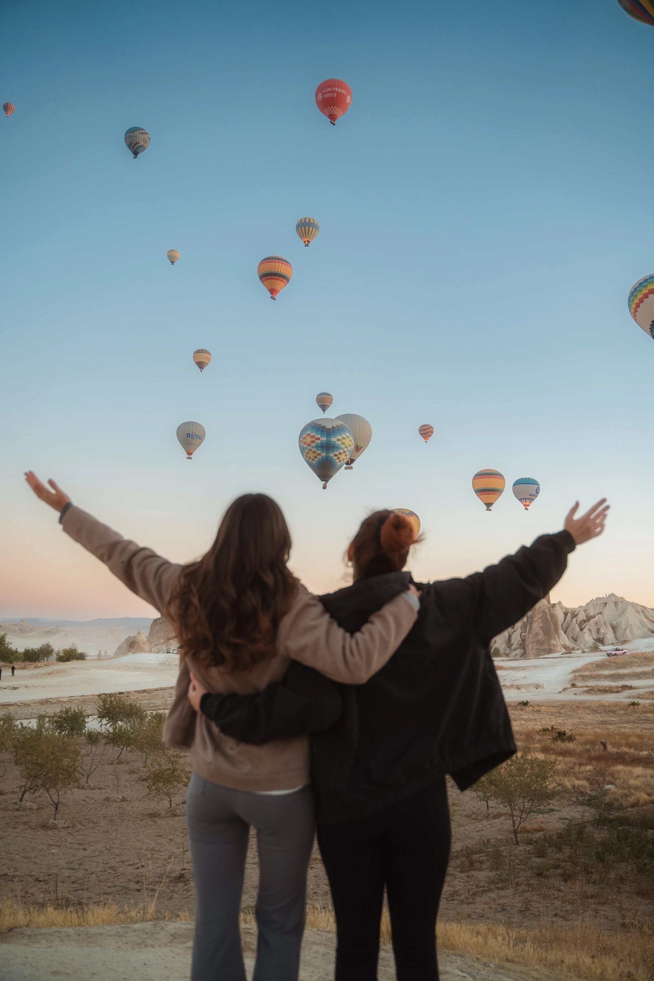 Zwei Frauen blicken Arm in Arm auf die Heißluftballons über Kappadokien.