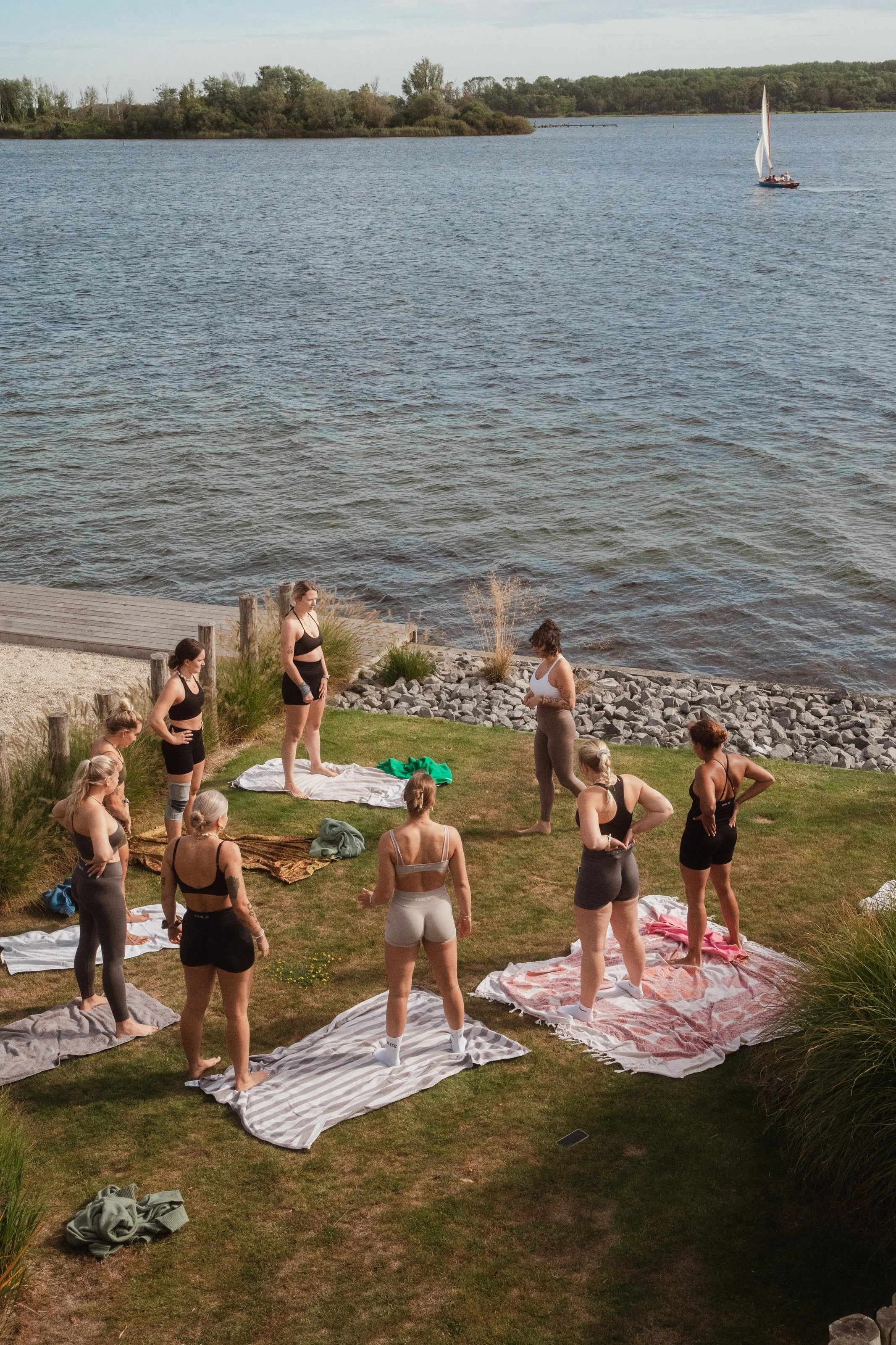 Eine Gruppe übt Yoga auf der Wiese am See, von oben gesehen.