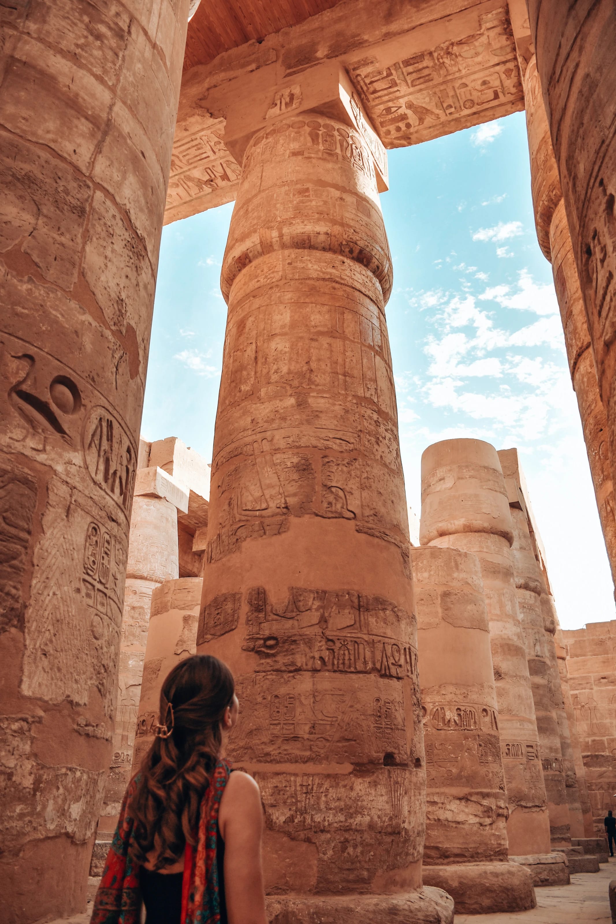 Eine Frau blickt zu den monumentalen, mit Hieroglyphen verzierten Säulen des Karnak-Tempels in Luxor hinauf.