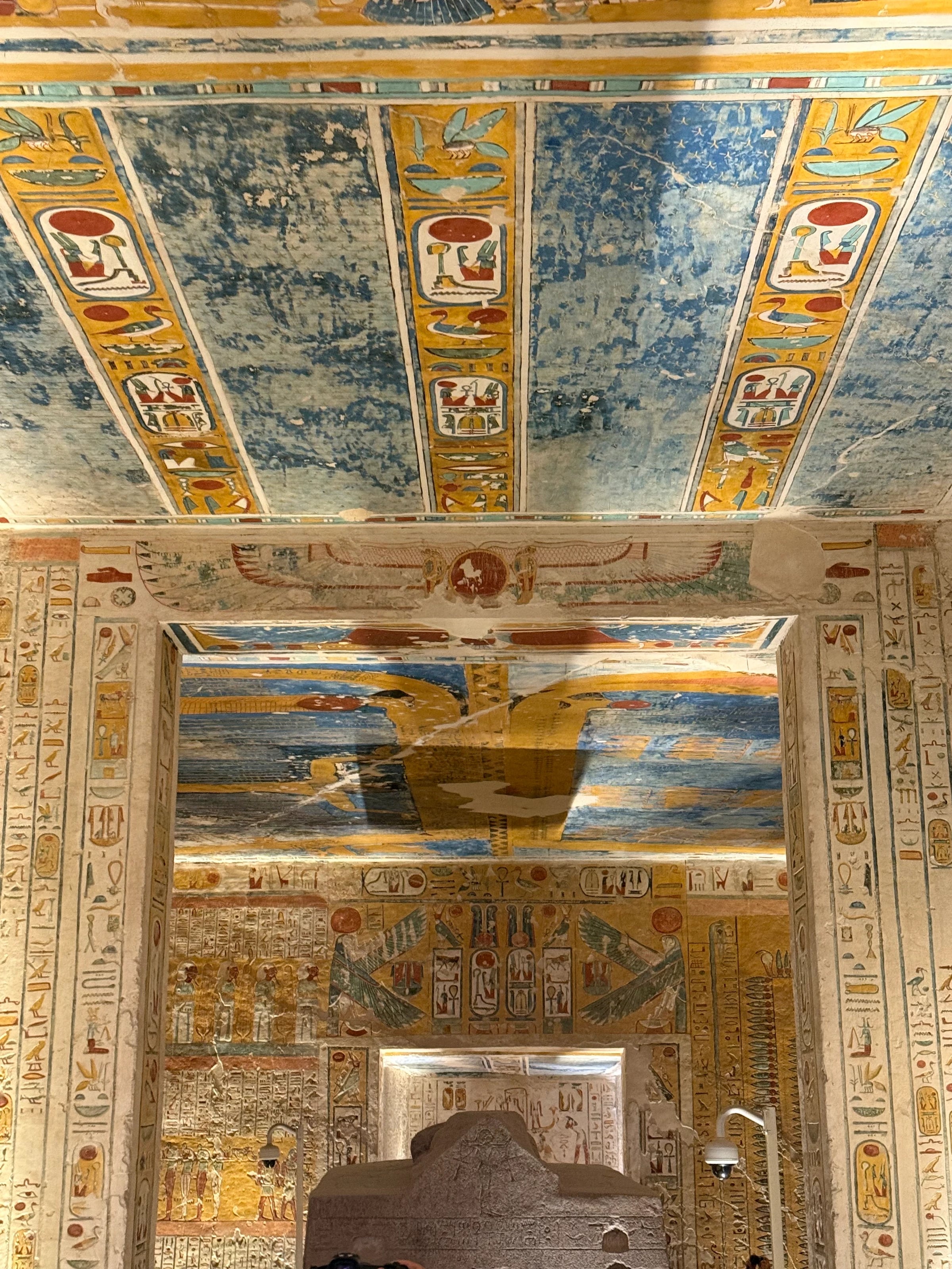 Eine blau-golden bemalte Grabdecke rahmt den Durchgang zu einem steinernen Sarkophag.