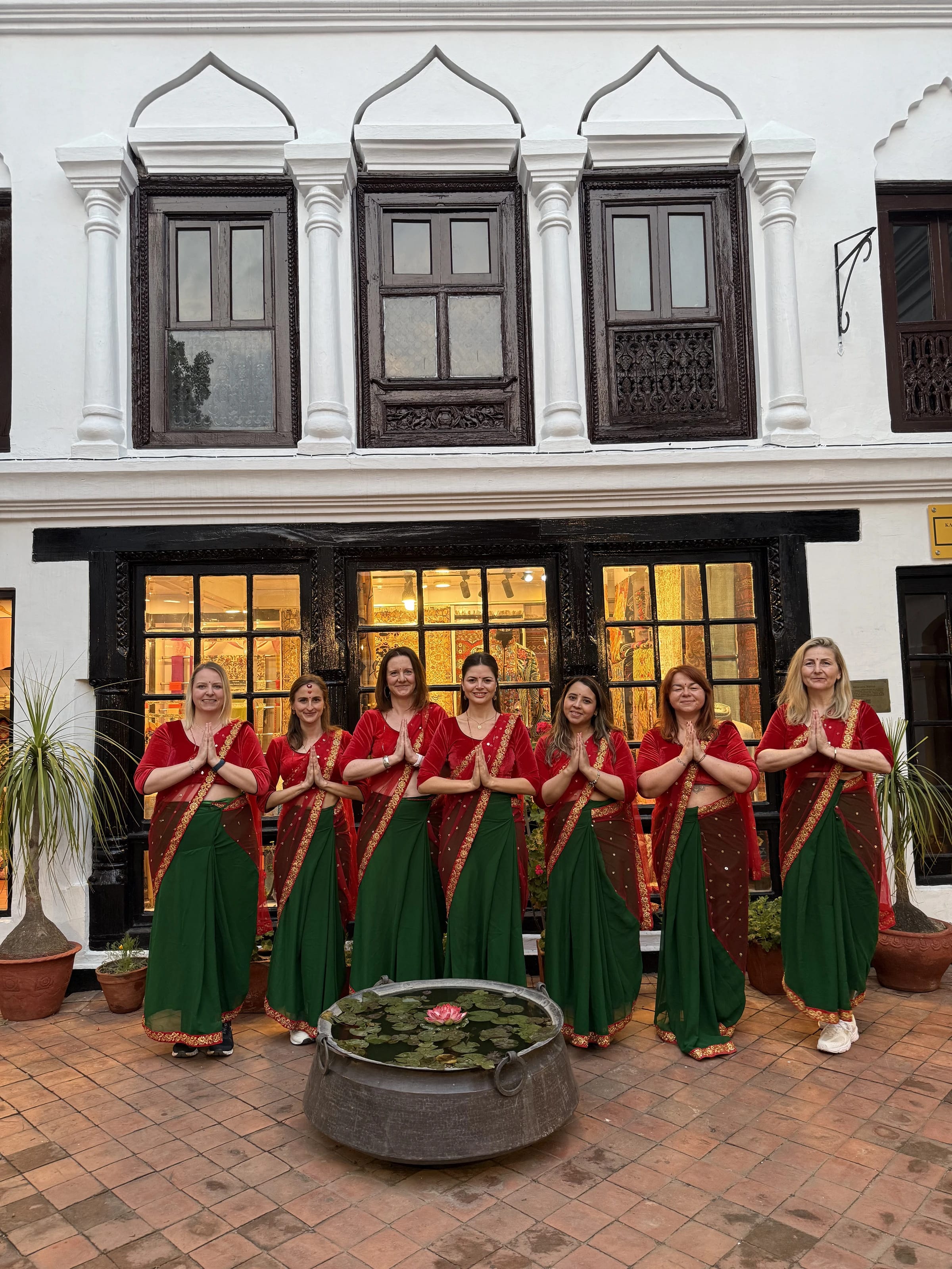 Die Reisegruppe steht in roten und grünen Saris mit der Namasté-Geste in einem Innenhof beim Willkommensessen.