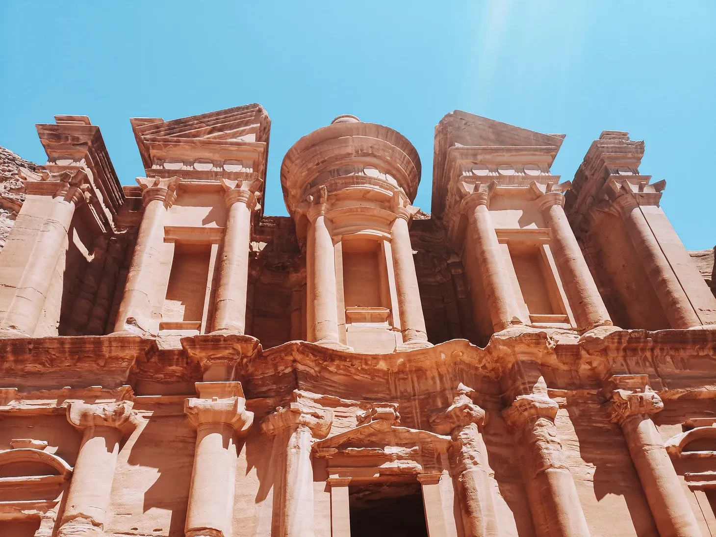 Nahaufnahme der geschnitzten Säulen und des Giebels des Ad-Deir-Klosters in Petra vor blauem Himmel.
