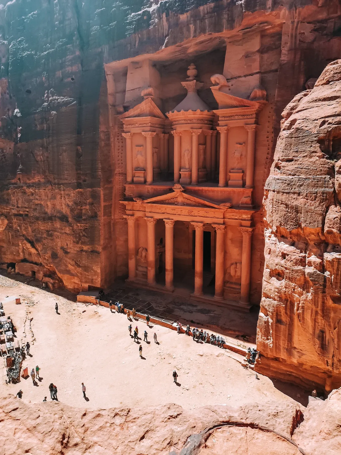 Blick von oben auf das Schatzhaus Al-Khazneh in Petra, in den Fels gehauen, mit kleinen Touristen im Vorplatz.