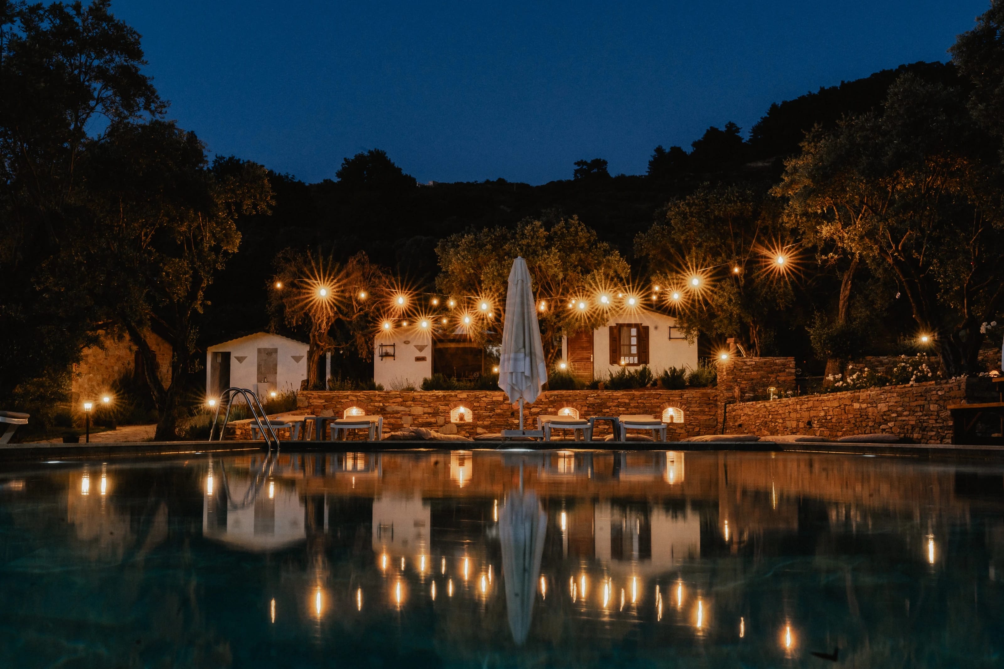Abendstimmung am Pool mit Lichterketten zwischen den Bäumen.