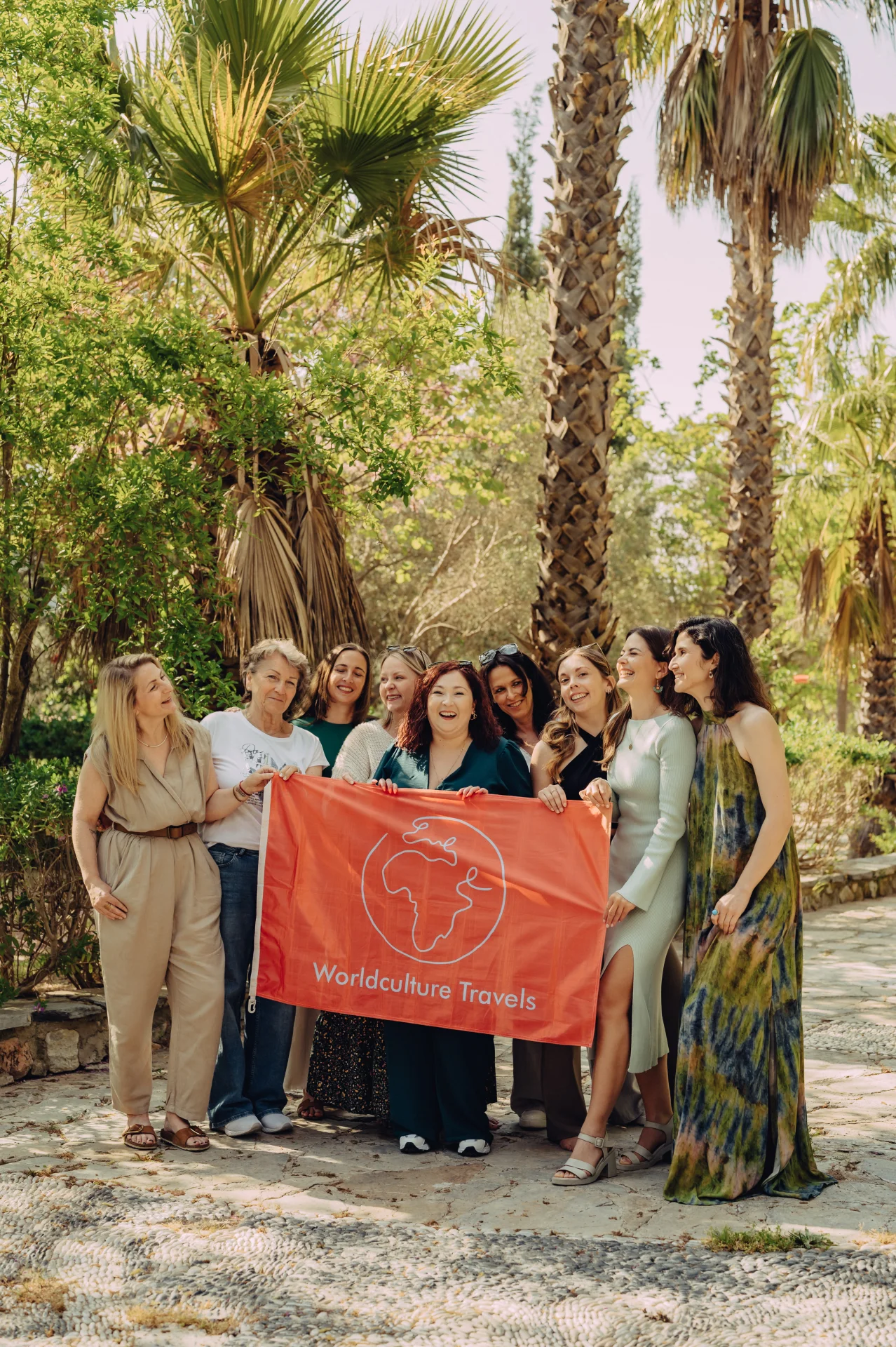 Die Frauen der WCT Community halten gemeinsam die orangefarbene Worldculture-Travels-Fahne zwischen Palmen